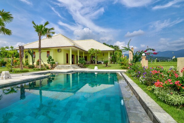 A house with a swimming pool, surrounded by lush greenery and a clear sky.