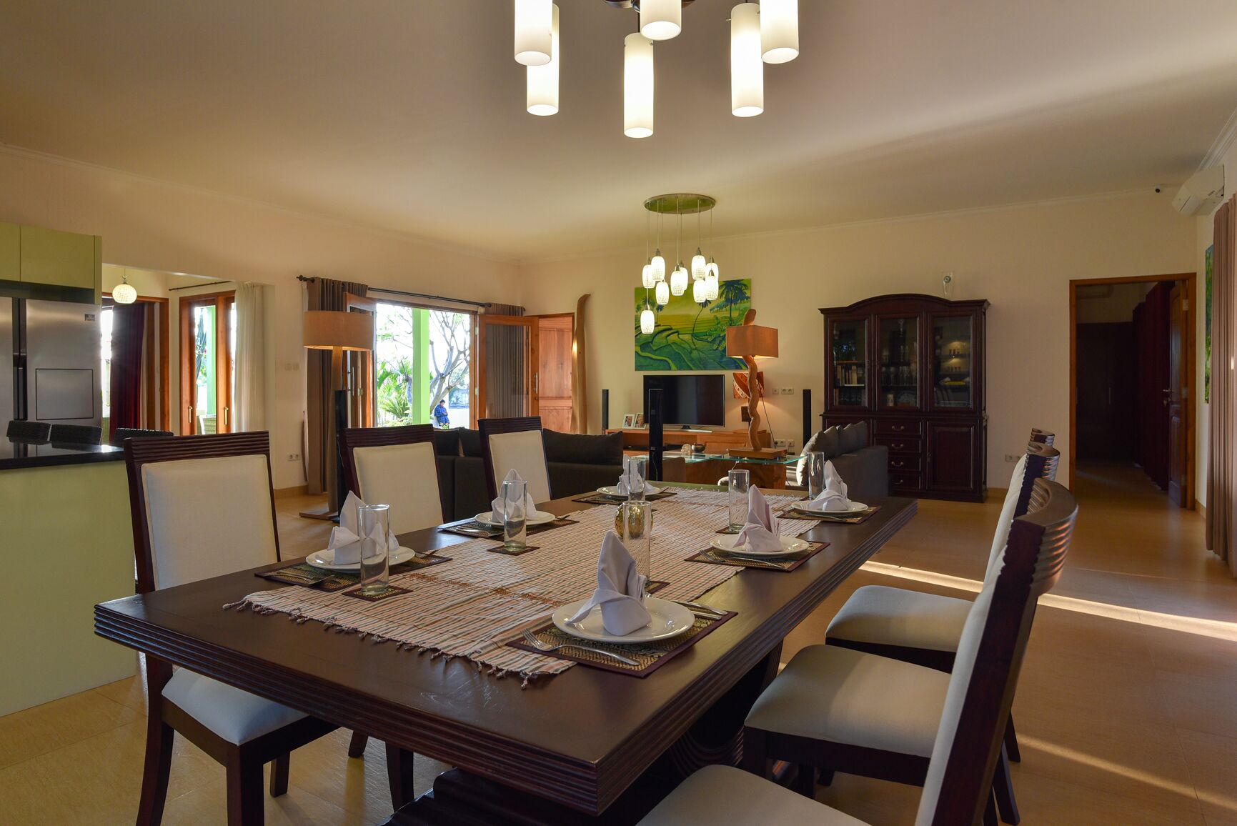 A dining area with a long table set for six, surrounded by chairs, with a television and artwork on the wall.