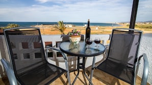 A balcony with two mesh chairs, a table with a bottle and glasses, and a view of the beach. - Irilena Apartments (Hersonissos)