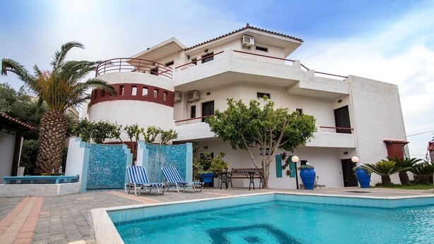 A two-story building with a swimming pool, palm trees, and a blue gate. - Irilena Apartments (Hersonissos)