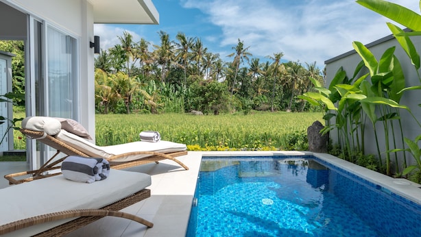 A modern outdoor pool area with lounge chairs, a clear blue pool, and lush greenery in the background. - Villa Shiva (Sukasada)