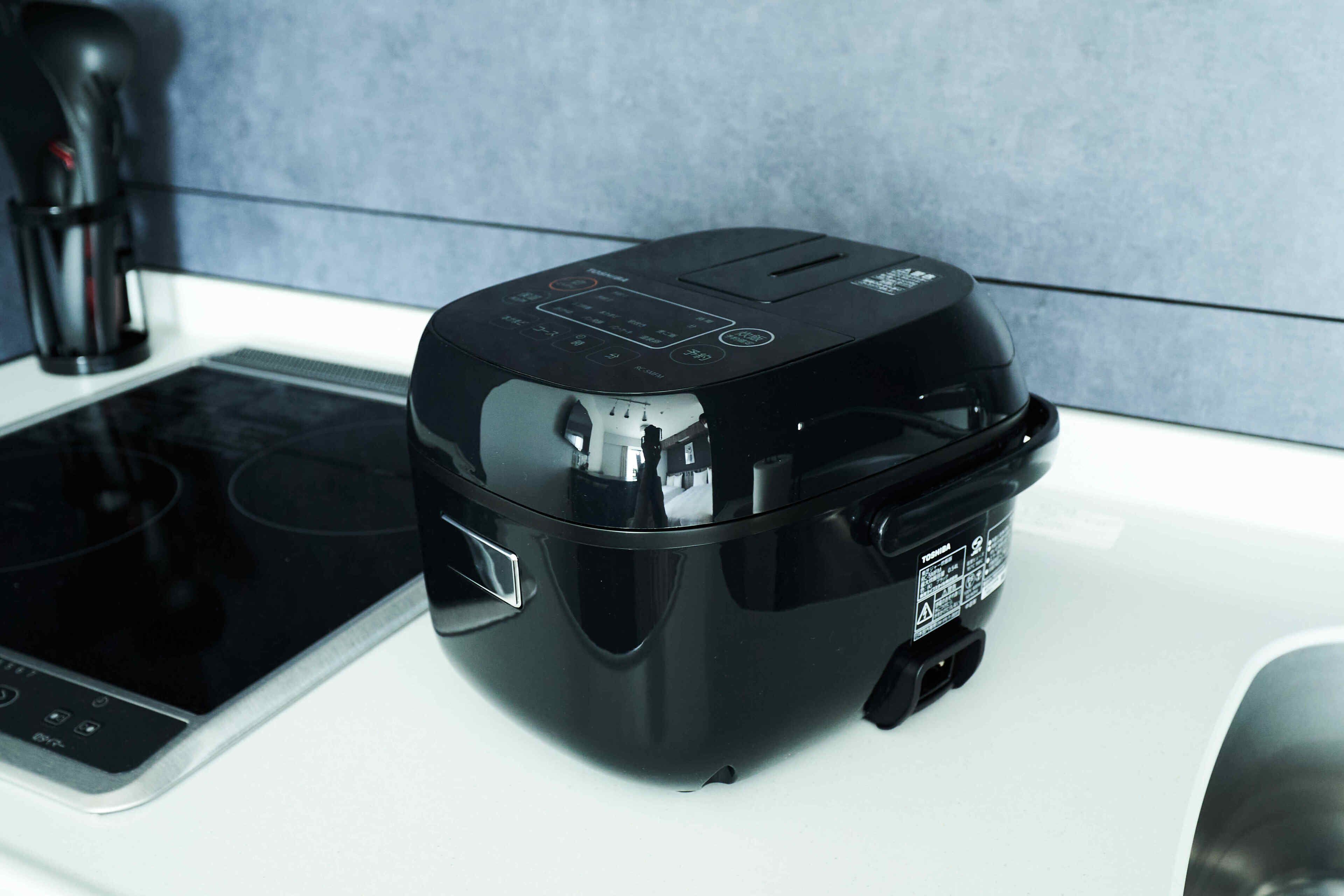 A black rice cooker on a white countertop next to a stove.