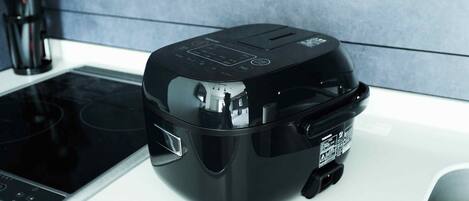 A black rice cooker on a white countertop next to a stove.