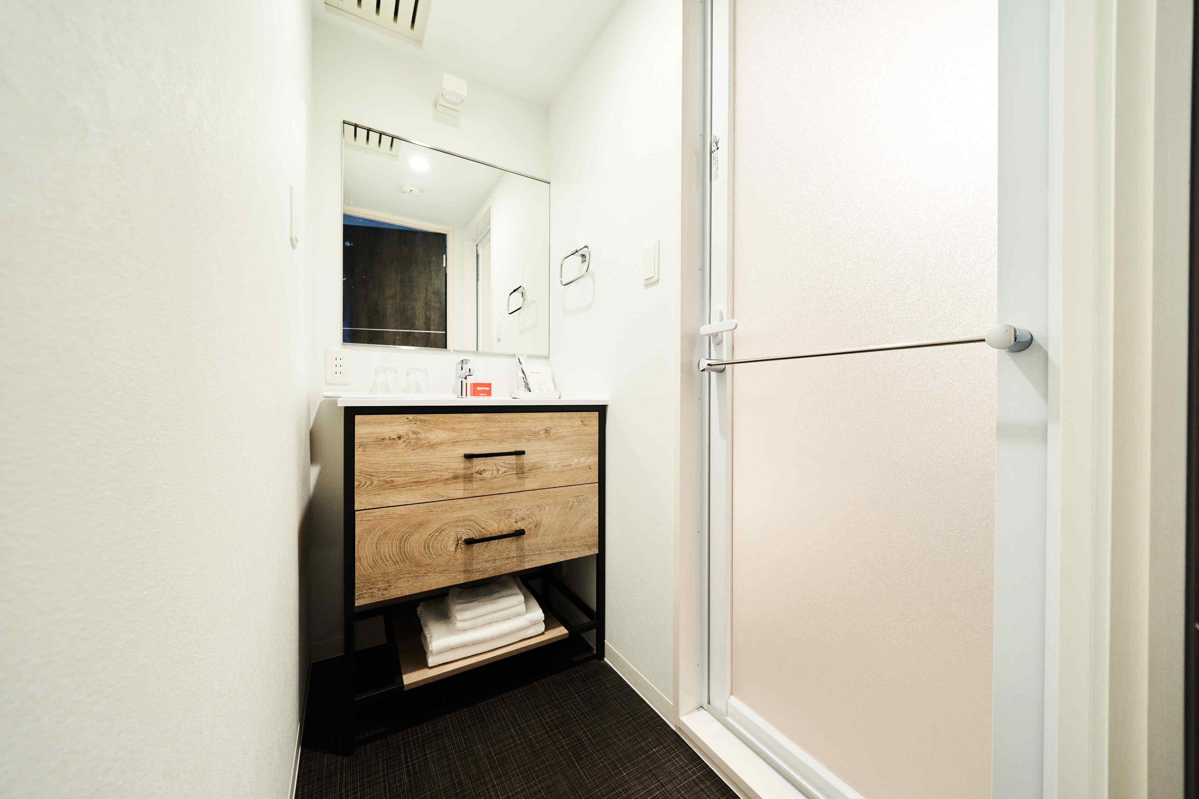 A small bathroom with a wooden vanity, a mirror, and a towel shelf.