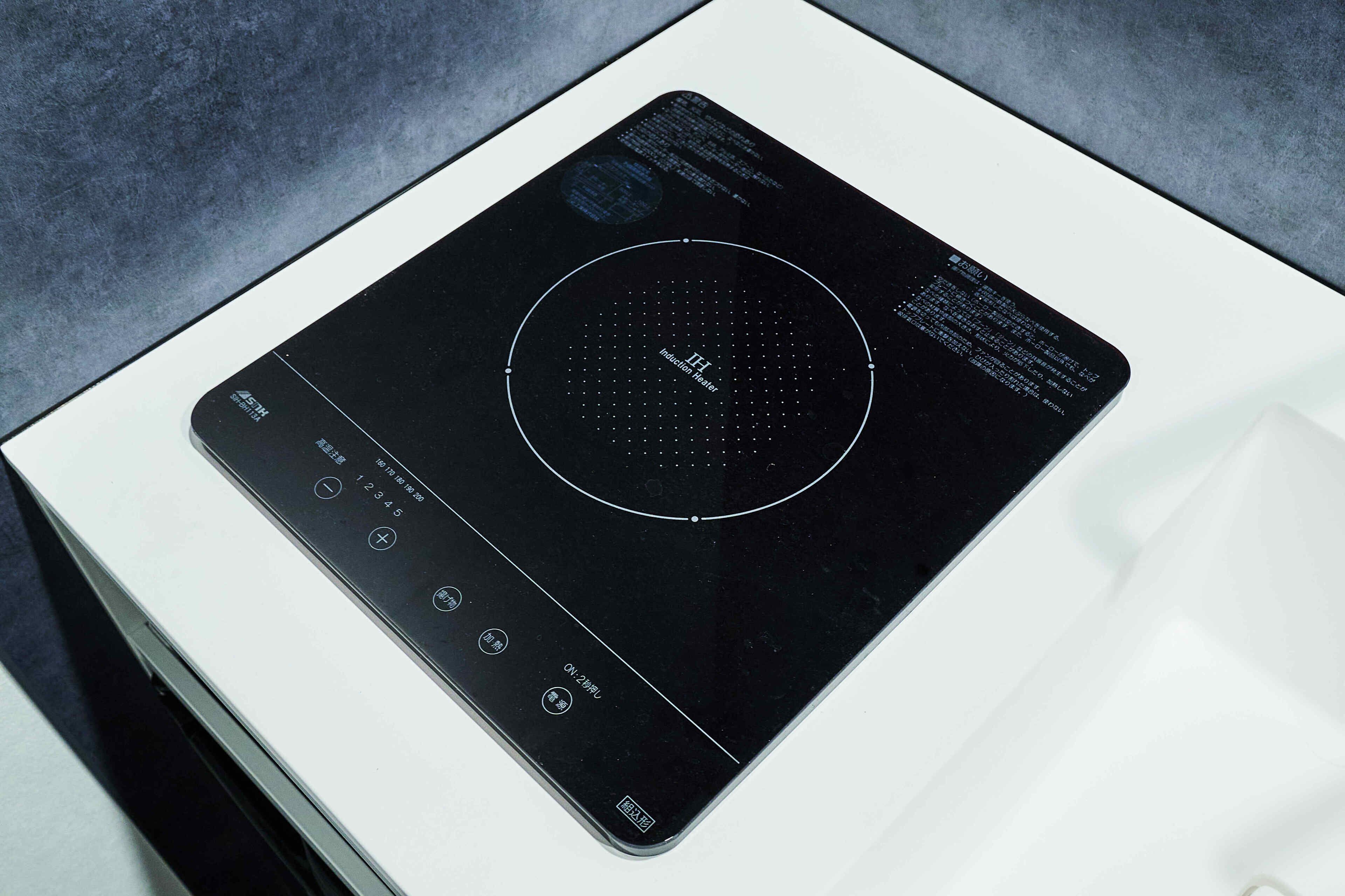 Una cocina de inducción negra con pantalla digital y botones de control sobre una encimera blanca.