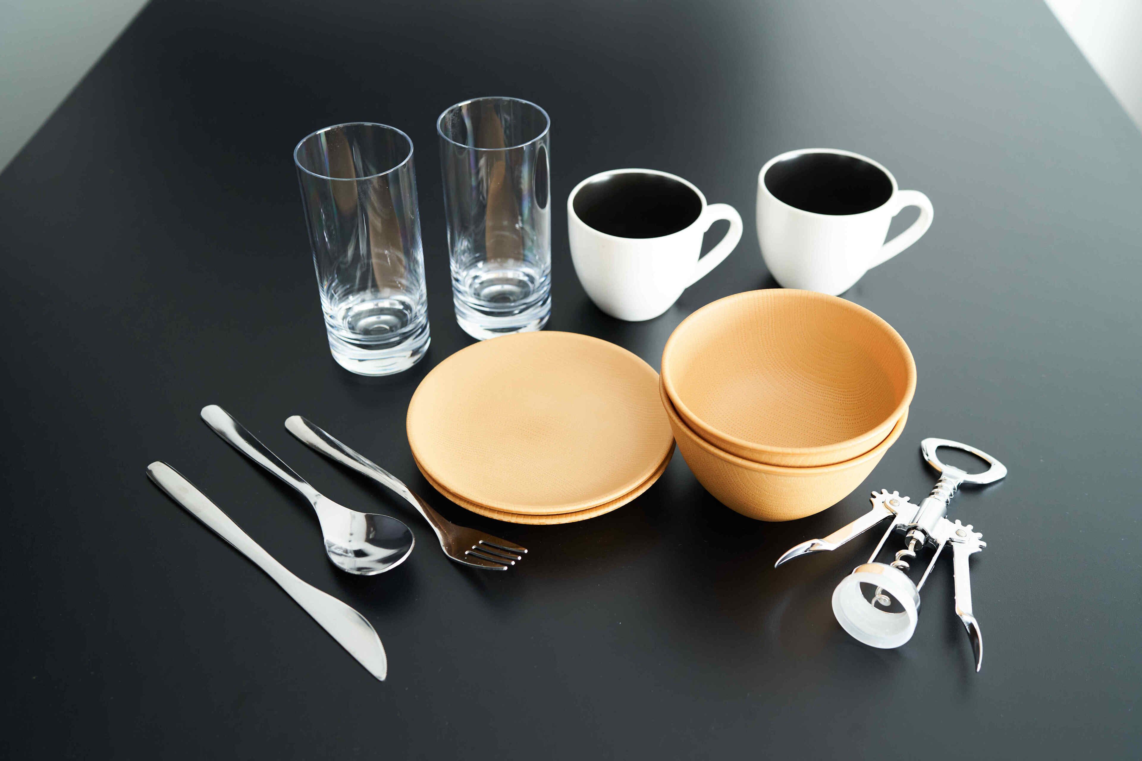 Una mesa con varios utensilios para comer, incluyendo platos, vasos, copas, cubiertos y un sacacorchos.