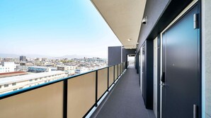 A corridor with a view of a cityscape, featuring a long hallway with doors on one side and a balcony with a railing on the other. - Grand STAY Hakata Station North (Fukuoka)