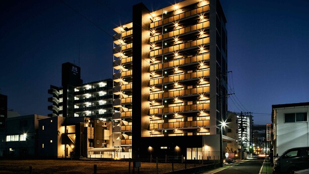 A modern multi-story building with illuminated windows and balconies, featuring a unique facade with geometric patterns. - Grand STAY Hakata Station North (Fukuoka)