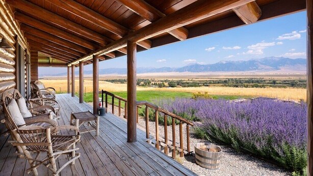 Une véranda couverte avec des poutres en bois, des fauteuils en osier et une vue sur un champ de lavande et les montagnes.