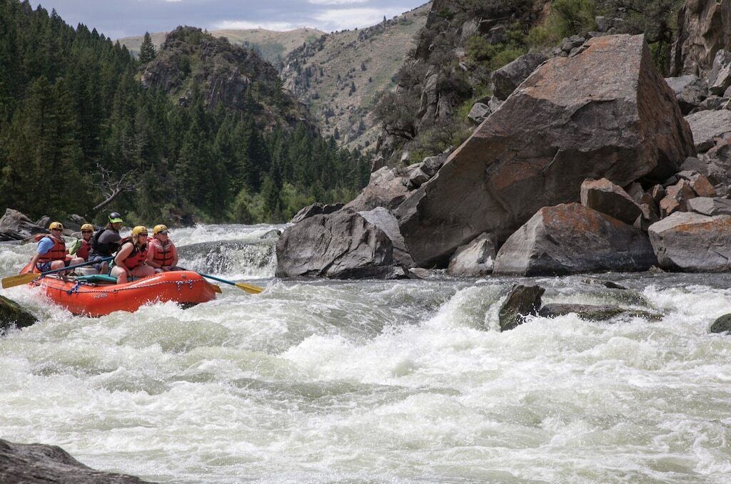 A group of people rafting down a river surrounded by rocky terrain and dense forest.