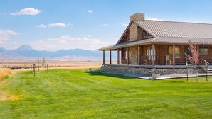 Une cabane en rondins avec des fondations en pierre, une véranda et une vue sur les montagnes en arrière-plan.