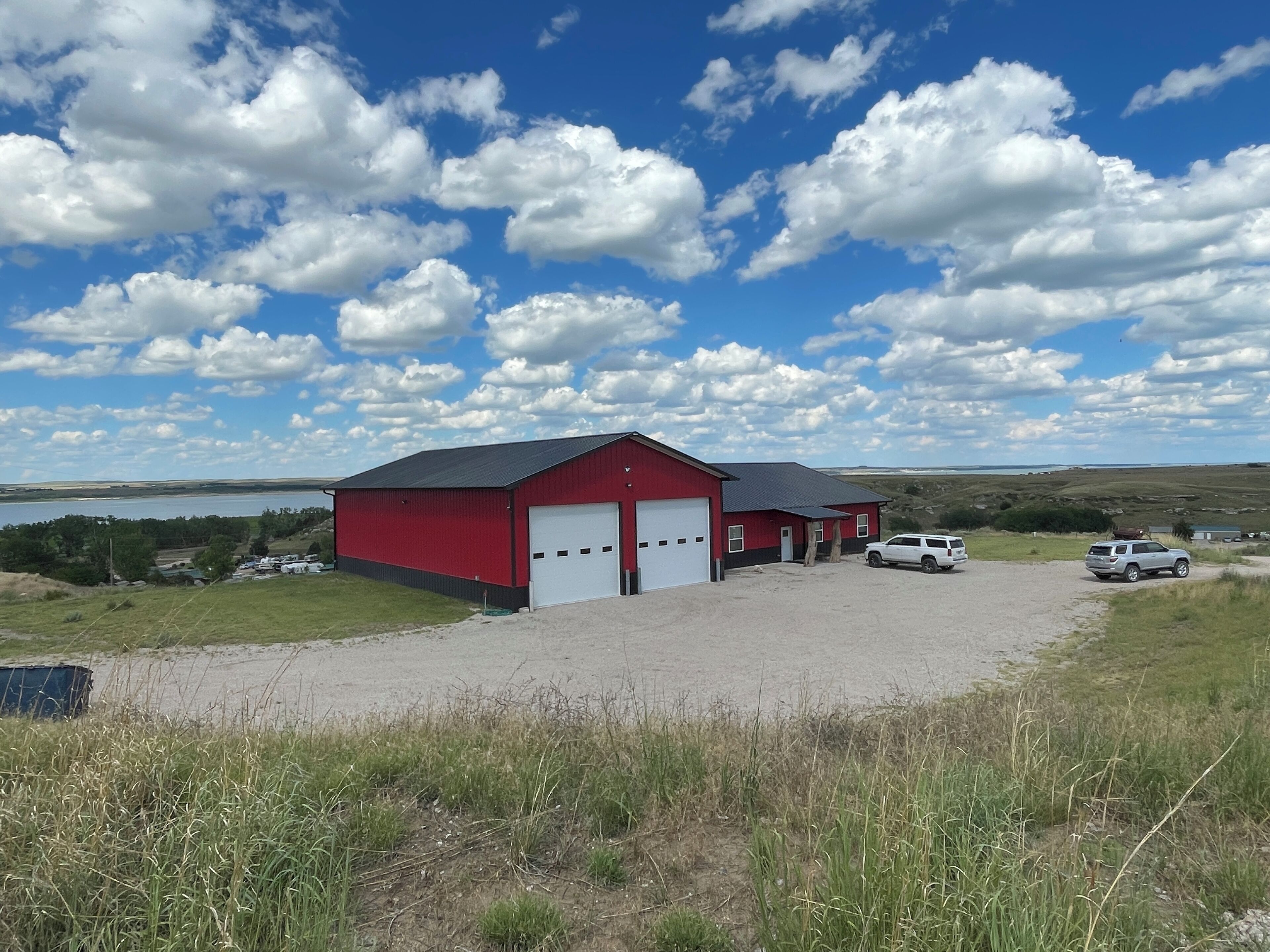 A red building with a garage, surrounded by a gravel driveway and parked vehicles.
