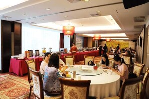 A hotel dining area with round tables, chairs, and a buffet setup.