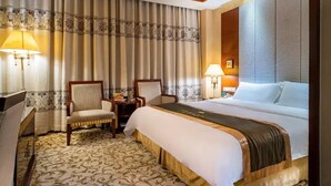 A hotel room with a large bed, two chairs, a small table, and a lamp. - Yijian Haoting Holiday Hotel (Zhuhai)