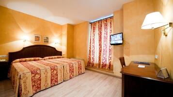 Una habitación de hotel con una cama grande, un escritorio, un televisor y una ventana con cortinas.