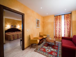 A hotel room with a bed, two armchairs, a coffee table, and a red sofa.