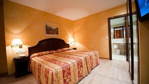 A hotel room with a large bed, two bedside lamps, a painting on the wall, and a view of the bathroom through a glass door. - Cordon (Burgos)