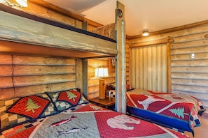 Une chambre de style cabane avec deux lits, des murs en bois, un lit superposé et une lampe.