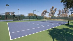 Un court de tennis avec un filet, entouré d’une clôture et équipé de projecteurs.
