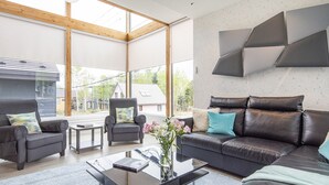 Una sala de estar moderna con techo de vidrio, sofás de cuero, una mesa de centro y vista a una casa exterior.