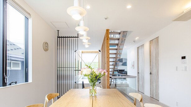 Un comedor moderno con una mesa de madera, sillas, un florero con flores y una escalera que lleva a un nivel superior.