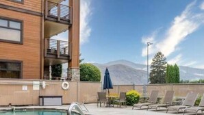 A pool area with a clear view of a mountain in the background, a wooden building with balconies, and outdoor seating. - Chelan Cabana Chalet (chelan)