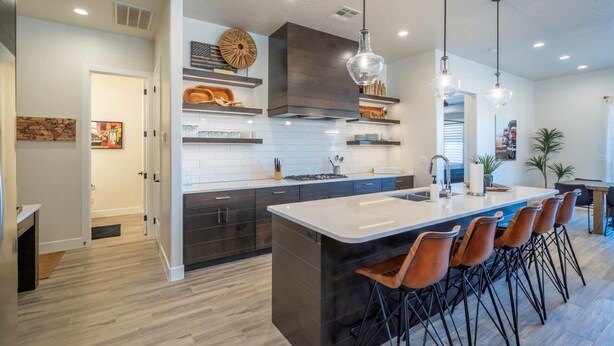 A modern kitchen with a large island, dark cabinetry, and pendant lighting.
