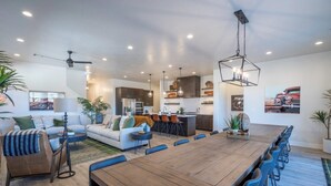 A spacious living area with a large wooden dining table, a sofa, and a kitchen in the background.