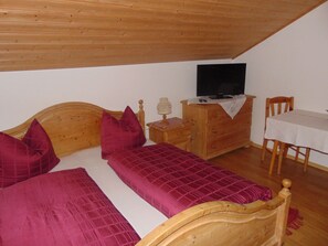 A bedroom with a wooden ceiling, a bed with a wooden headboard, a dresser, a television, and a small table with a chair. - Abendsonne Apartment: Sleeps up to 5, balcony, 51 m² (Taching am See)
