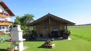 Una cabaña de madera con un porche, una chimenea de piedra y un pequeño jardín con flores y un bebedero para pájaros.