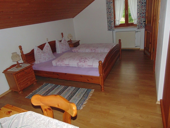 A bedroom with a wooden bed, a nightstand, a chair, and a window with curtains. - Abendsonne Apartment: Sleeps up to 5, balcony, 51 m² (Taching am See)