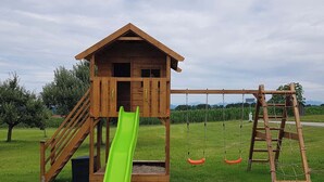 Una casita de juegos de madera con un tobogán y columpios.