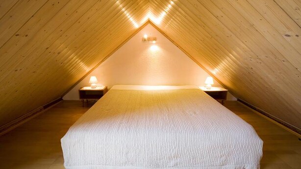 Een knus slaapkamer onder het dak, met een schuine wand, een groot bed en twee bedlampjes.
