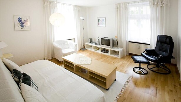A modern hotel room with a bed, a wooden coffee table, a TV, a black chair, and a radiator. - Charming Apartment "Bregenz 6 Top 1" in Central Location with Wi-Fi, Terrace & Garden (Bregenz)