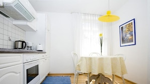 A kitchen with white cabinets, a coffee maker, a kettle, and a dining table with chairs. - Charming Apartment "Bregenz 6 Top 1" in Central Location with Wi-Fi, Terrace & Garden (Bregenz)