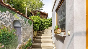 A stone wall with a door, a staircase leading to a wooden building, and a window on the right. - Cozy Holiday Apartment "Alina" with Garden Seating, Wi-Fi, Non-Smoking (Singen)