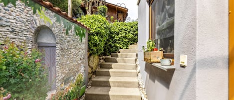 Un muro de piedra con una puerta, una escalera que conduce a un edificio de madera y una ventana a la derecha.