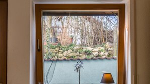 A window with a view of a garden, a potted plant, and a lamp on the windowsill. - Cozy Holiday Apartment "Alina" with Garden Seating, Wi-Fi, Non-Smoking (Singen)