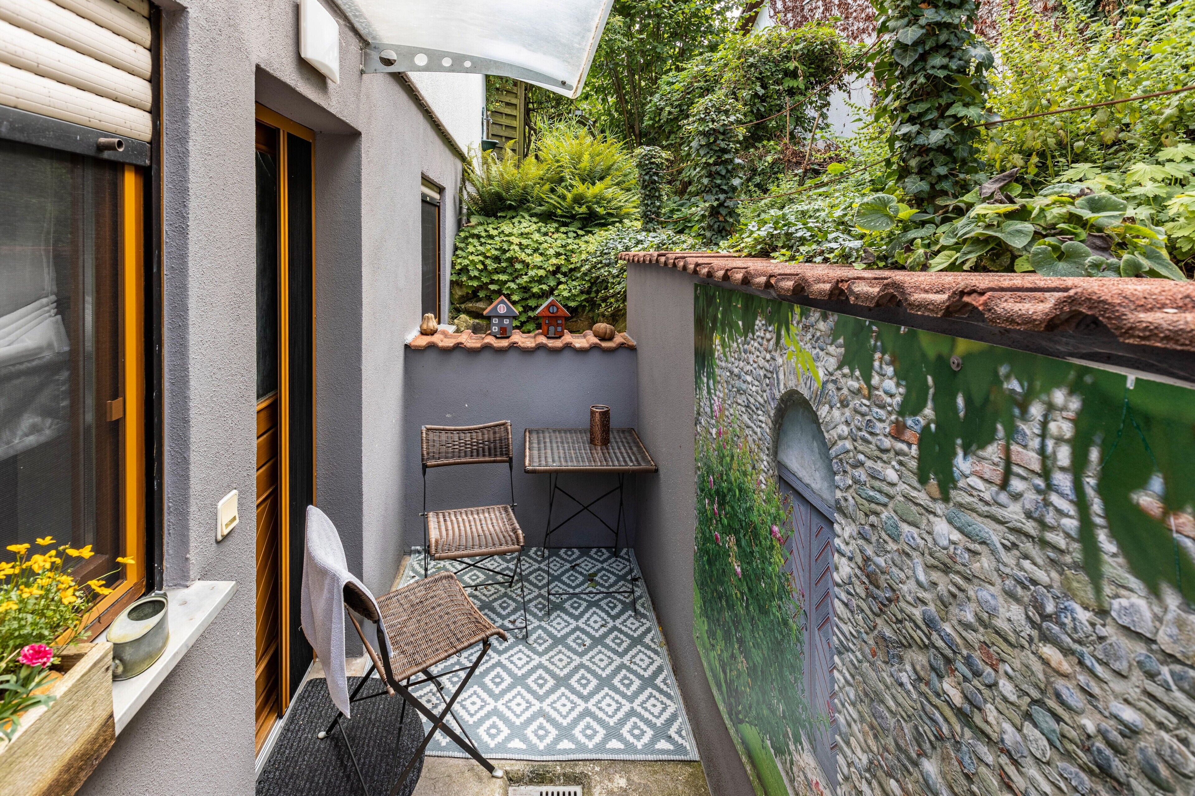 Eine kleine Terrasse mit Tisch und Stühlen, einem Blumentopf und einer Zierwand.