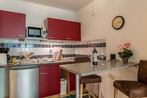 Una cocina con armarios rojos, un microondas, un lavamanos y un reloj en la pared.