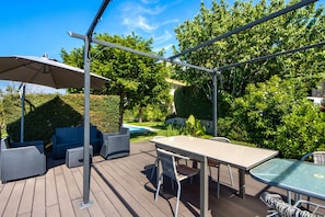 Terraza al aire libre con mesa y sillas, un espacio de estar cubierto y una piscina al fondo.