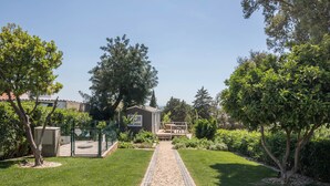 A paved pathway leading to a building with a deck, surrounded by greenery and trees. - Cabana Garden House with Shared Pool, Panoramic View & Wi-Fi (Loulé)