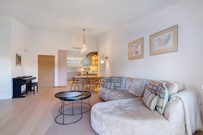 Een moderne woonkamer met een hoekbank, een ronde salontafel, een piano en een eethoek op de achtergrond.