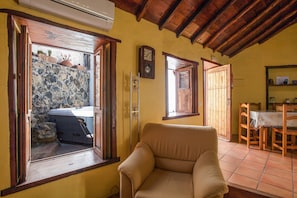 A cozy room with a stone wall, a wooden ceiling, a sofa, a dining table with chairs, and a clock on the wall.