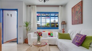 A living room with a white sofa, a wooden coffee table, a window with blue shutters, and a painting on the wall. - Vacation Home 'Rosa' with Private Terrace, Private Garden and Wi-Fi (Yaiza)