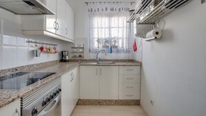 A kitchen with white cabinets, a stove, a sink, and a window with a curtain. - Vacation Home 'Rosa' with Private Terrace, Private Garden and Wi-Fi (Yaiza)