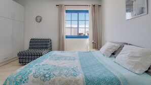 A bedroom with a bed, a chair, a window with curtains, and a wall-mounted picture. - Vacation Home 'Rosa' with Private Terrace, Private Garden and Wi-Fi (Yaiza)