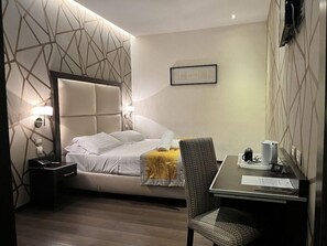 A hotel room with a bed, bedside table, chair, desk, and a wall-mounted TV. - Catone District Hotel (Rome)