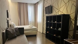 Una habitación de hotel moderna con sofá, cama, televisor y estantería.