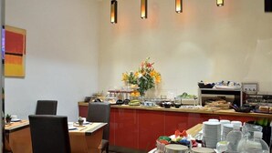 Un área de desayuno con mostrador, mesas de comedor y diversas opciones de comida y bebida.